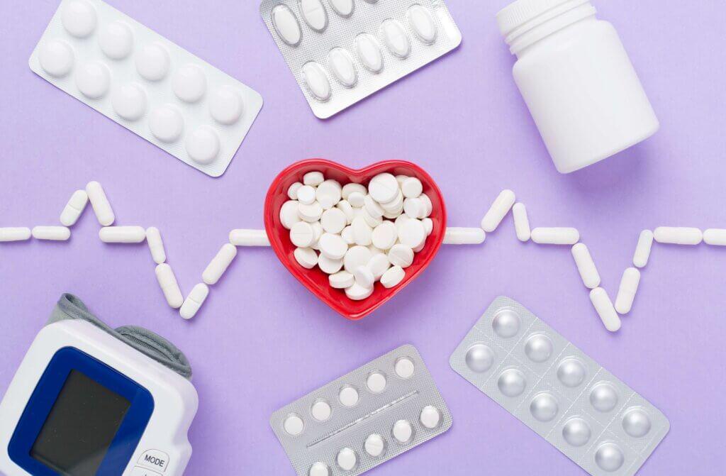 Cardiogram made with medicines and heart-shaped bowl on color background, top view