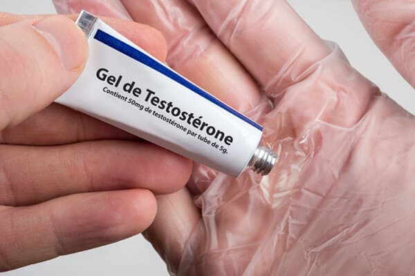 Une main appuie sur un petit tube portant l'inscription « gel de testostérone ».