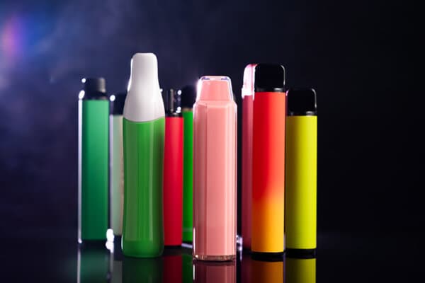 Un ensemble de cigarettes électroniques jetables colorées de différentes formes sur un fond noir avec de la fumée.