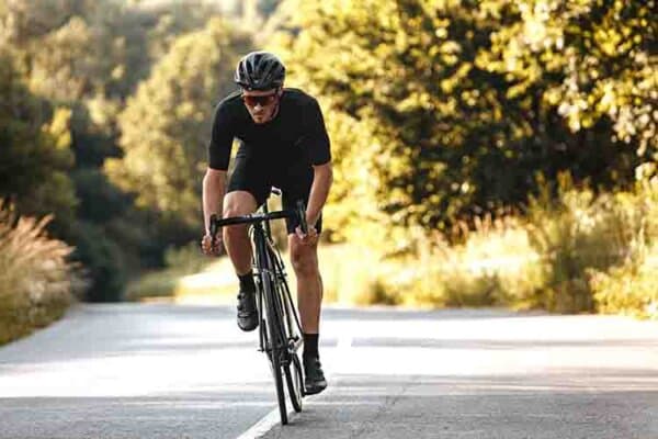 Ein Mann mit Fahrrad-Kleidung und -Helm fährt mit dem Fahrrad eine Strasse hoch.