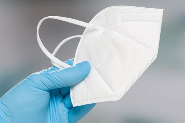 Hand mit chirurgischen blauen Handschuhen hält eine Schutzmaske.
