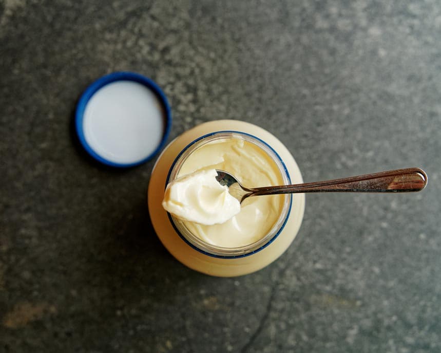 EIn Glas Mayonaisse obendrauf ein Löffel gefüllt mit Mayonnaise daneben der Deckel zum Glas