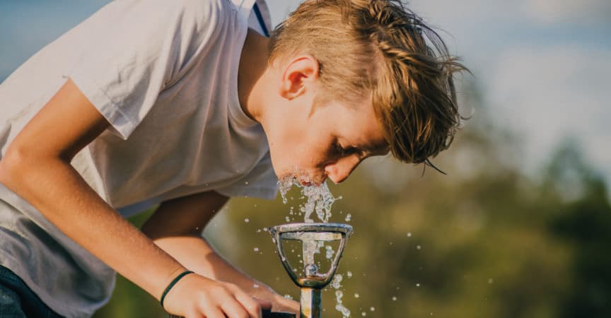 Kleiner Junge trinkt aus einem Brunnen in einem Park in Melbourne, Australien.