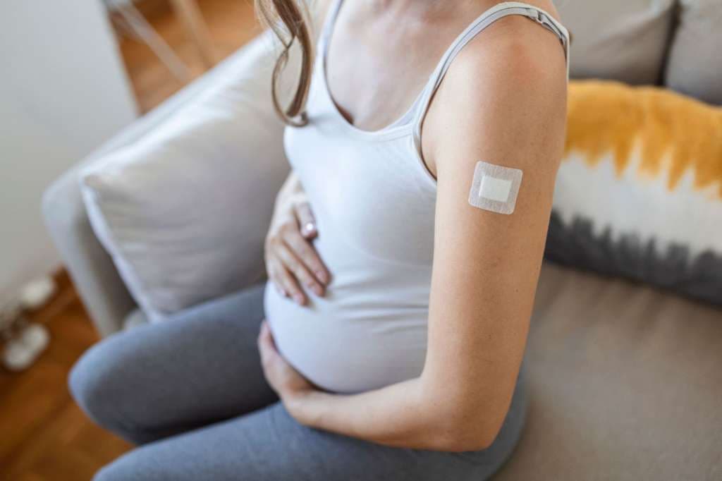 Schwangere Frau zeigt geimpften Arm mit Pflaster nach der Injektion des Coronavirus Impfstoff