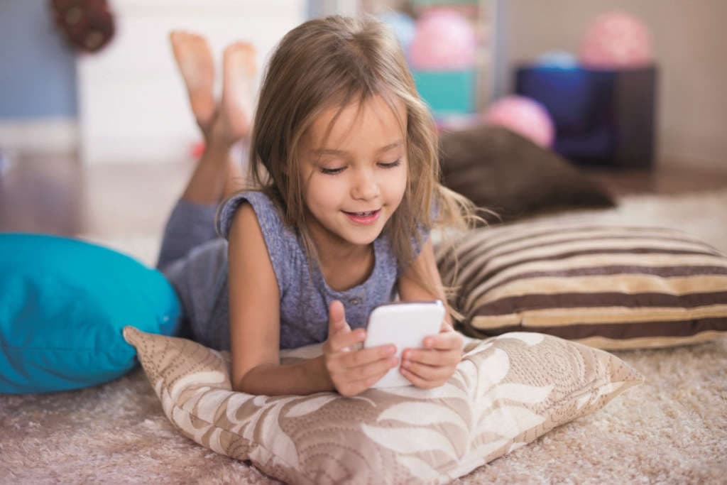 ein kleines Kind mit einem Smartphone auf dem Bett