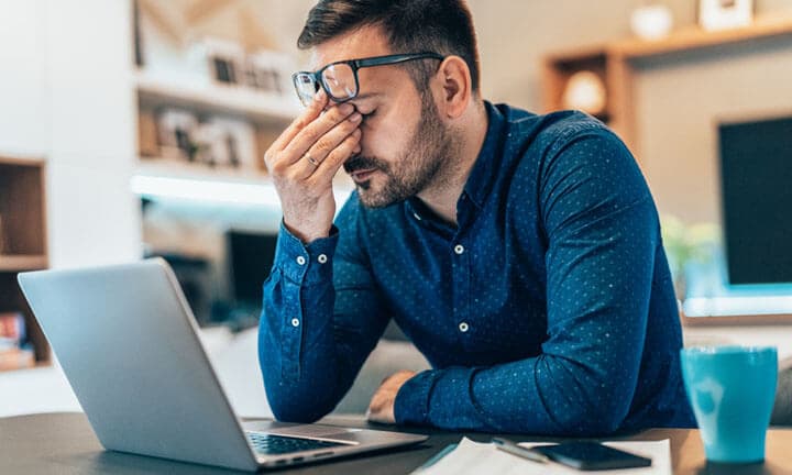 Tired young businessman working at home using lap top and looking Anxious