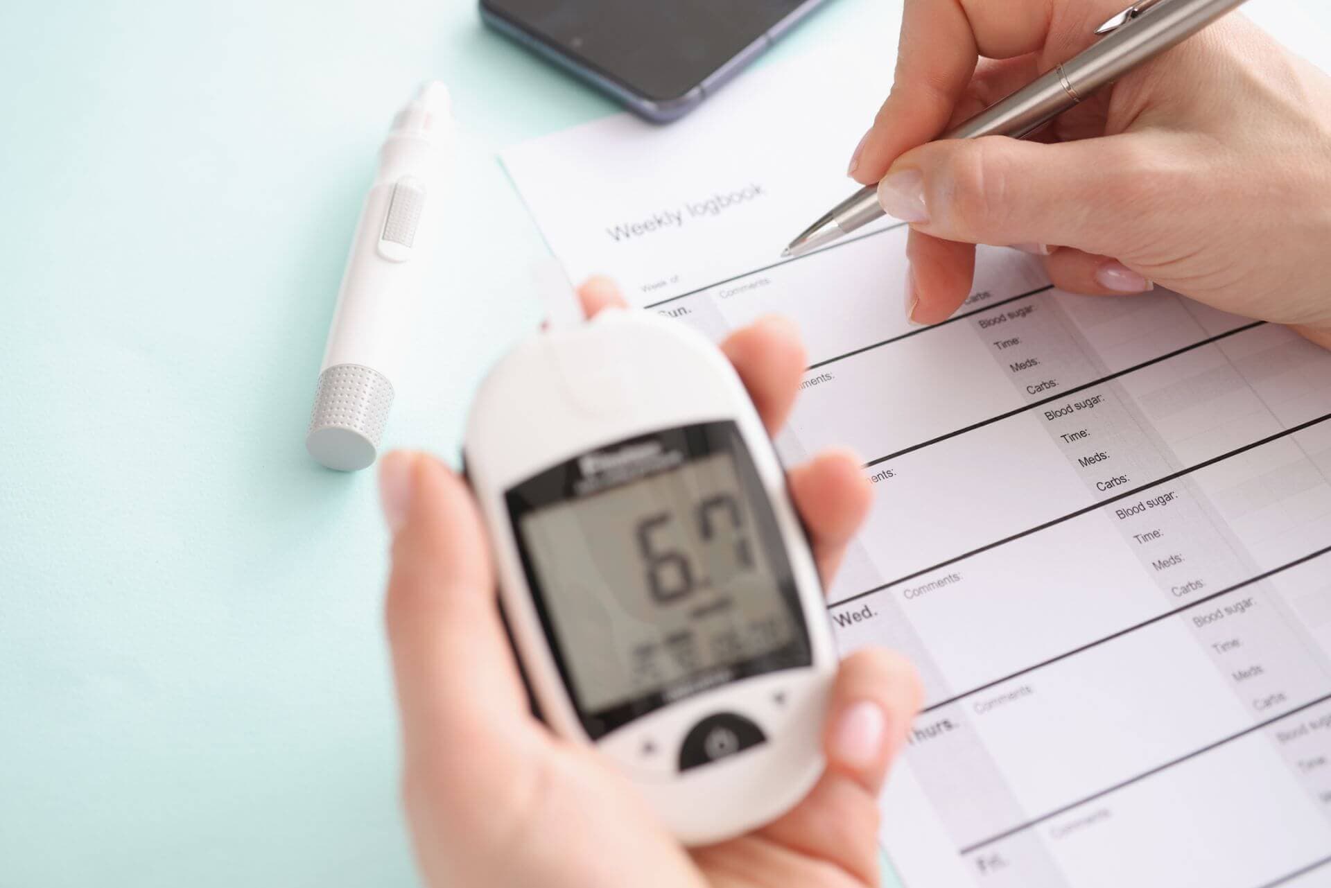 Glucometer with blood test results in patient hand fills in results in daily report. Diabetes mellitus concept