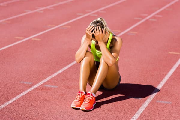 Frustrierte Sportlerin sitzt auf einer Tartanbahn und vergräbt das Gesicht in den Händen.