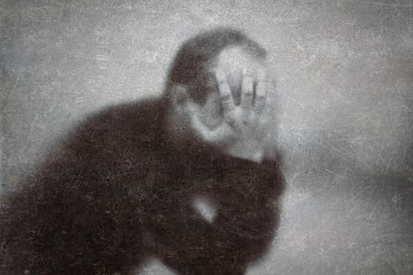 Ein depressiver, gebrochener Mann hinter zerkratztem Glas hält verzweifelt den Kopf in seine Hände,