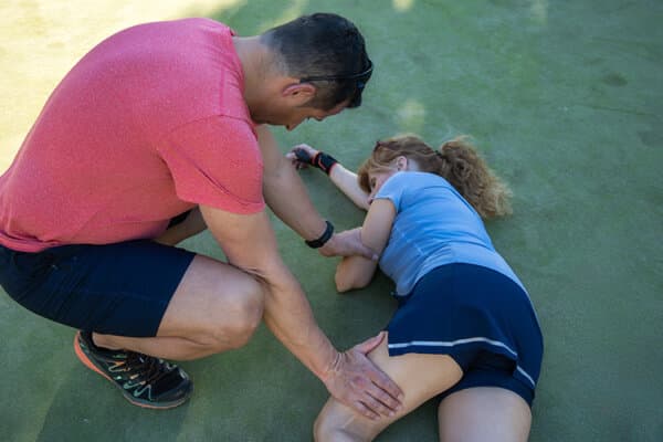 Un homme évalue la blessure d'une jeune athlète allongée sur un terrain de sport.