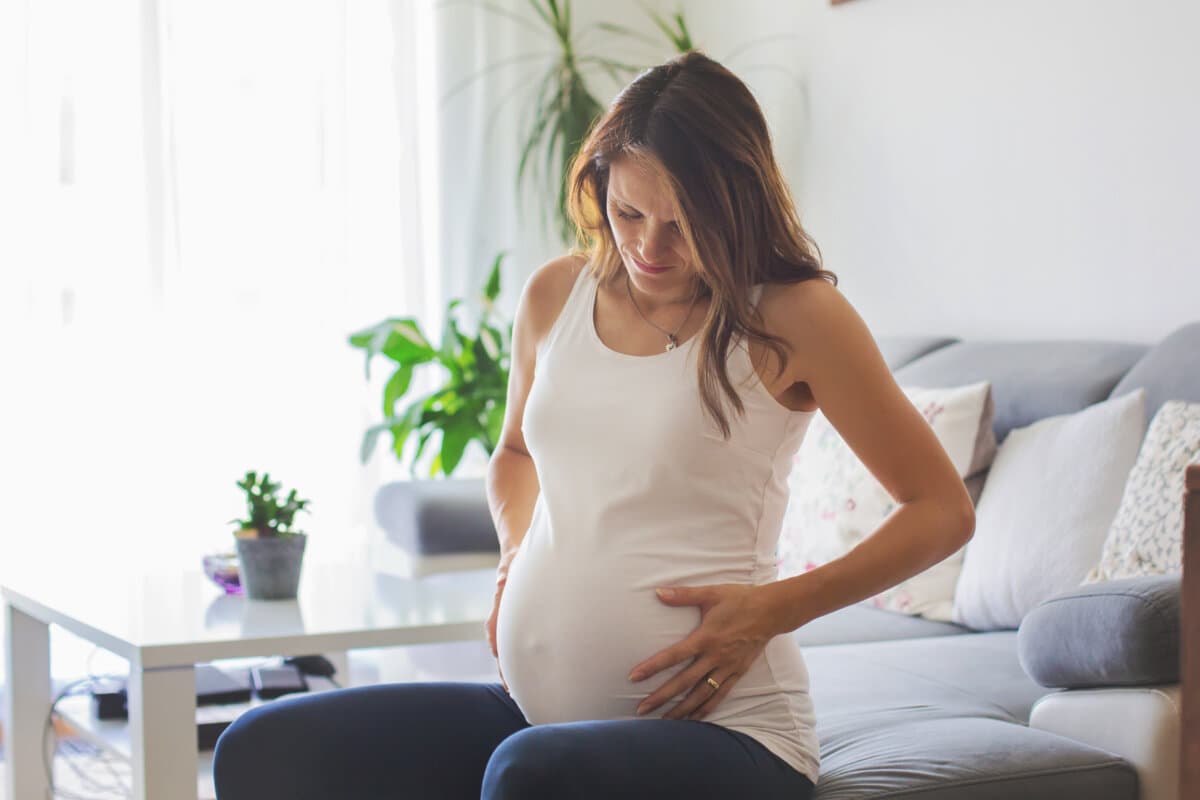 Jeune femme enceinte, ayant des contractions douloureuses, début du travail, assise sur le canapé