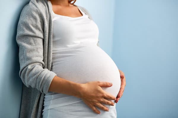 Porträt einer nicht zu erkennenden Frau in den letzten Monaten der Schwangerschaft, die sich in einem Zimmer an eine blaue