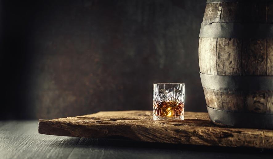 Glas Whisky neben einem Vintage Holzfass auf einem rustikalen Holz und dunklem Hintergrund