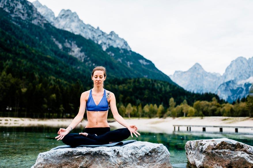 Frau mach Yoga sitzend auf einem grossen Felsen am See