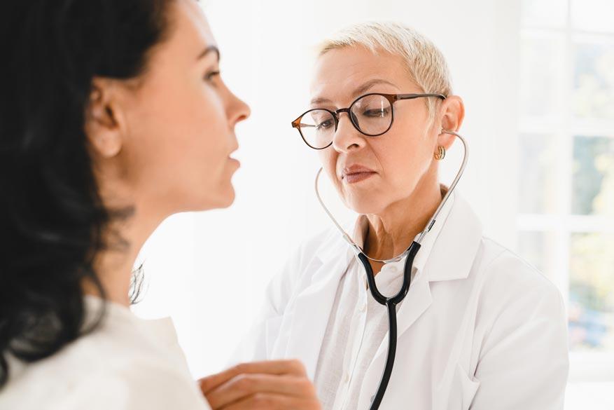 Ärztin hört mit Stethoskop die Lunge einer Frau ab