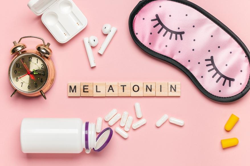 Buchstaben Melatonin, Wecker, weisse Flasche und Pillen und eine Schlafmaske auf hellem Hintergrund