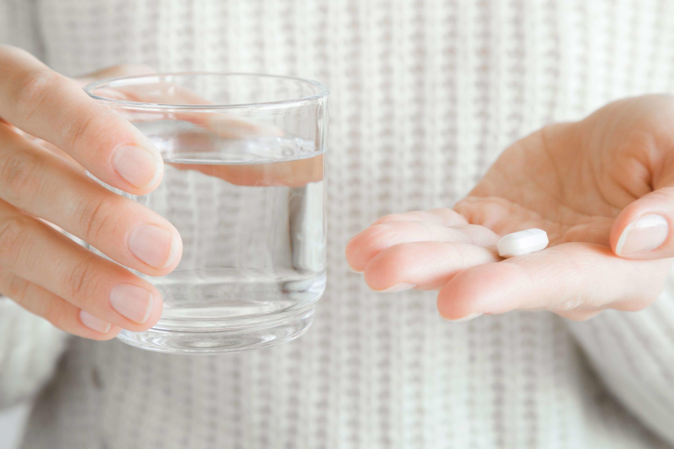 Frauenhände, die ein Glas Wasser und weiße Pille halten. Vitamine erhalten. Medizin-, Apotheken- und Gesundheitskonzept.