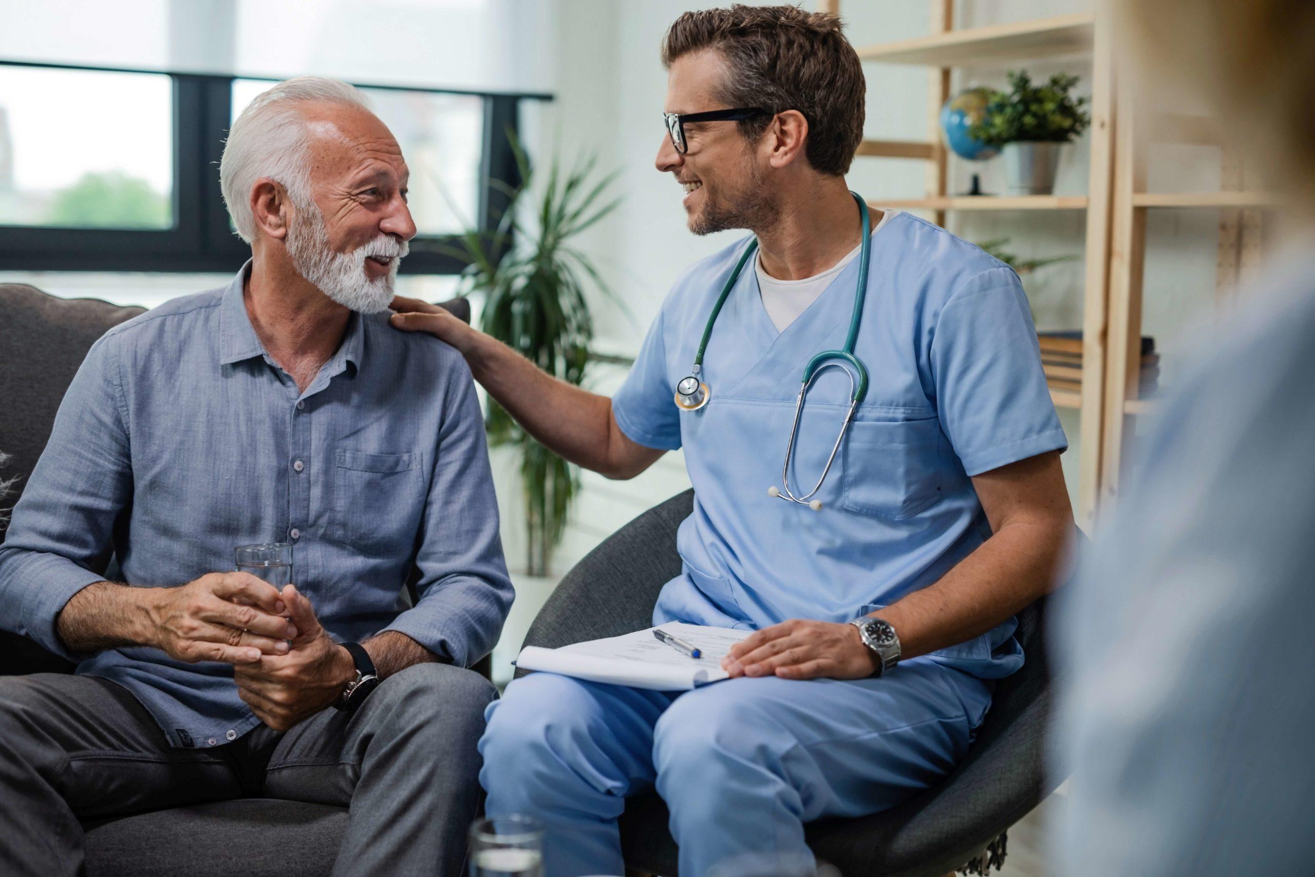 Glücklicher Arzt, der mit älteren männlichen Patienten während eines Hausbesuchs spricht.