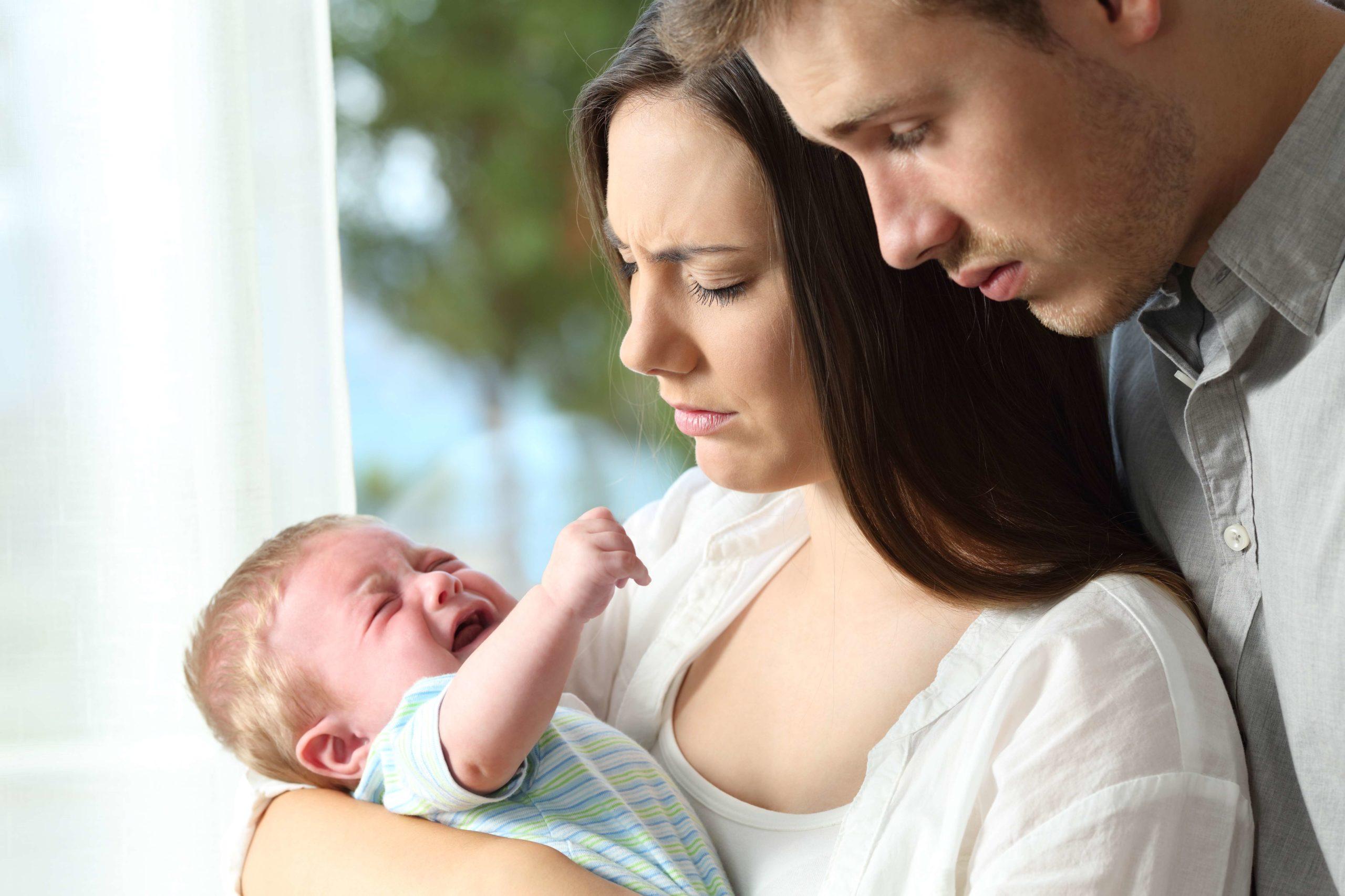 Müde verzweifelte Eltern halten ihr Baby zu Hause und weinen verzweifelt
