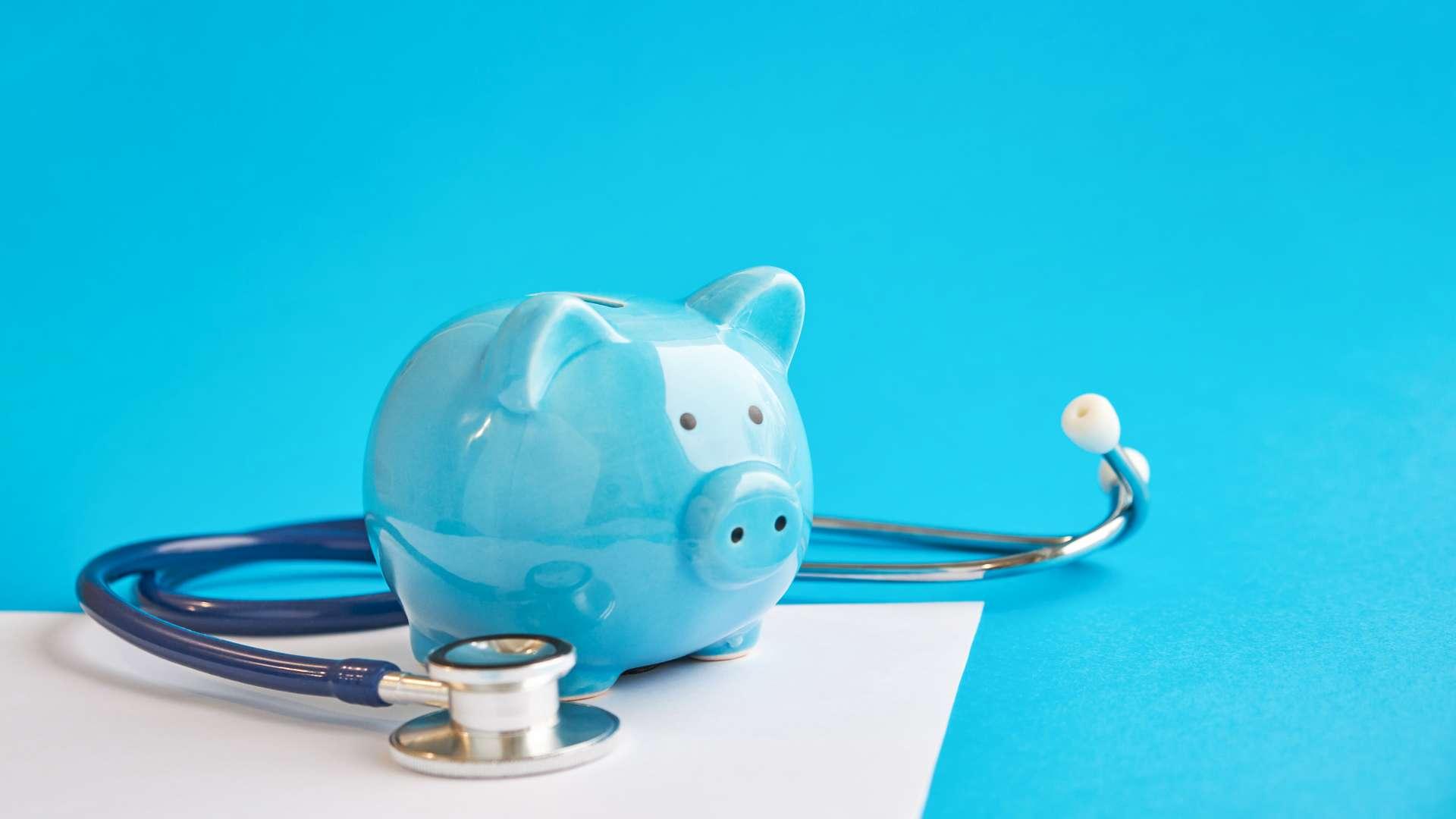 Sparschwein mit Stethoskop lokalisiert auf blauem Hintergrund. Steuervergleichskonzept. Medizinische Kostenabzüge und Steuererleichterungen