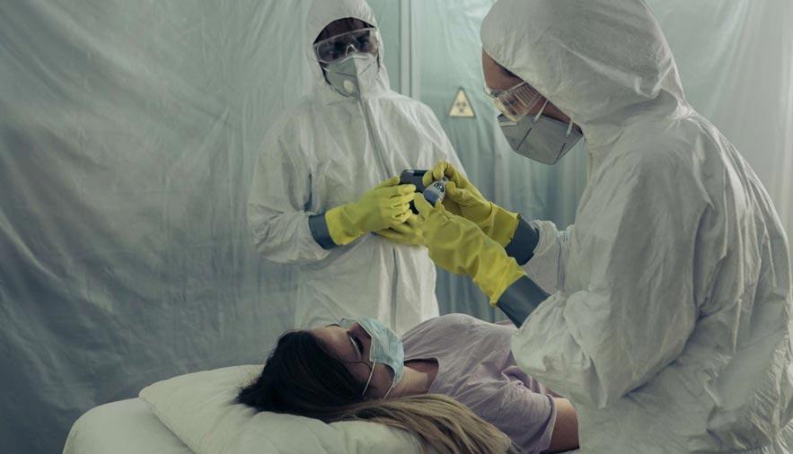 Zwei Ärzte im Schutzanzug betreuen eine Frau auf dem Bett