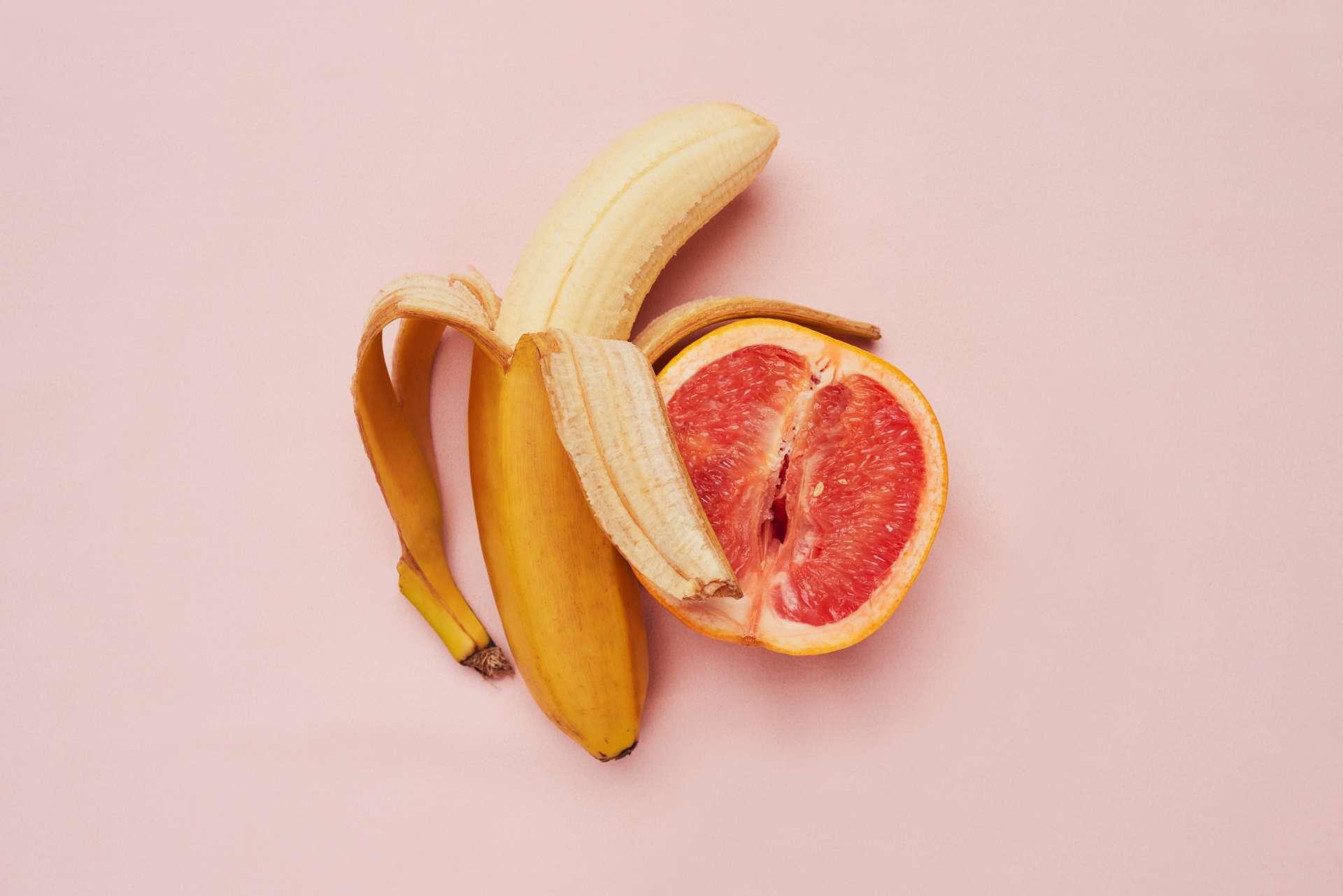 Studioaufnahme einer Banane und einer Grapefruit in einer suggestiven Position vor einem rosa Hintergrund