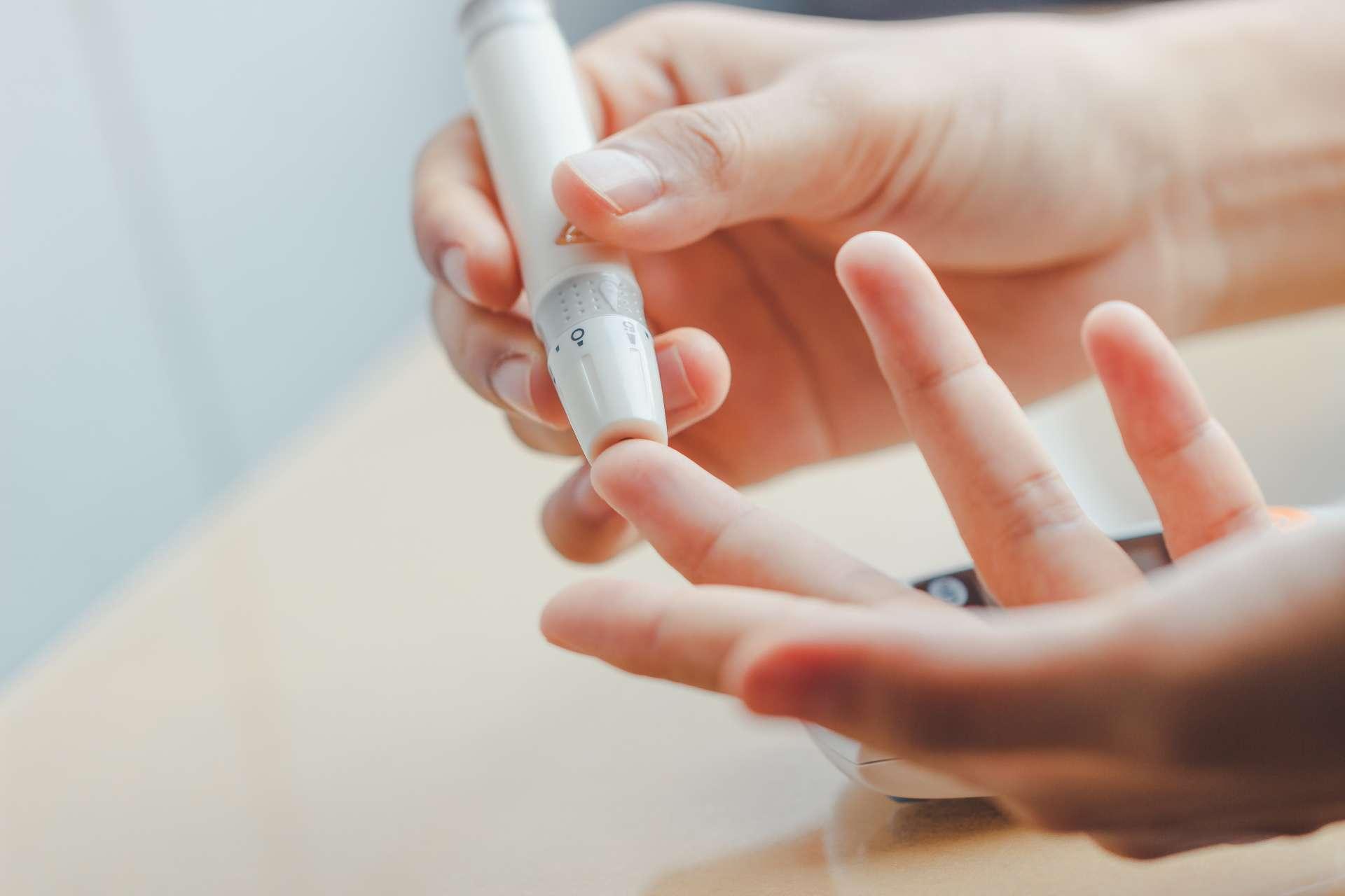 Nahaufnahme von Frauenhänden unter Verwendung der Lanzette am Finger, um den Blutzuckerspiegel durch Glukosemessgerät unter Verwendung als Medizin zu überprüfen