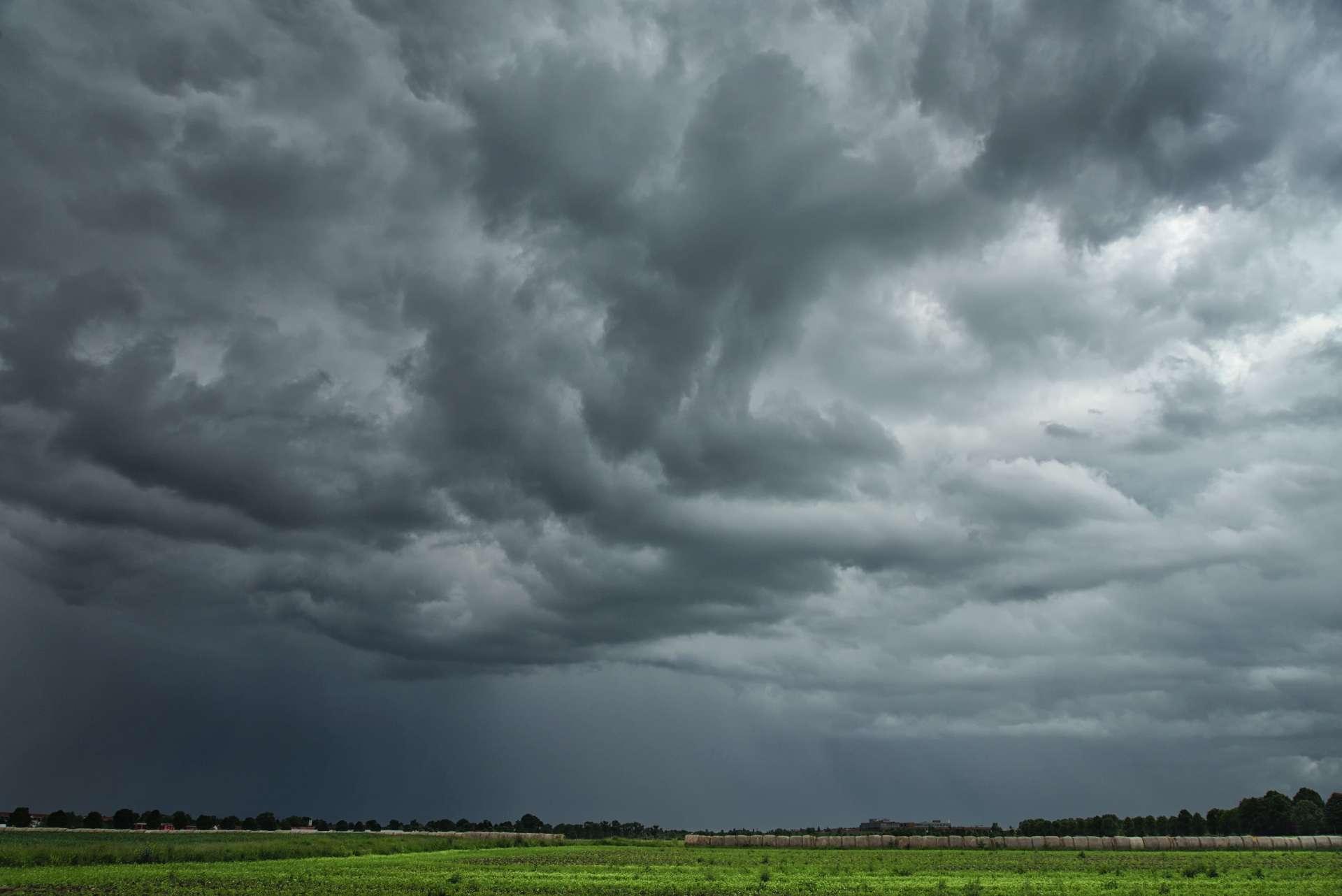 Dunkle, bedrohliche Wolken ziehen über eine sommerliche, ländliche Landschaft und bringen heftigen Regen mit Gewittern.