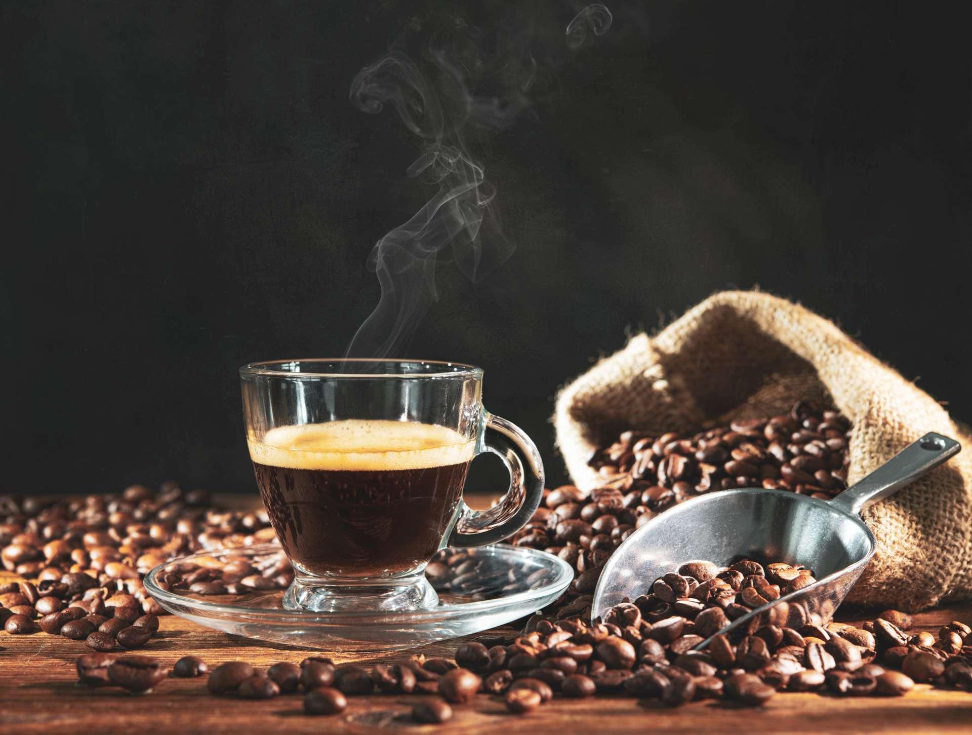 Tasse Espresso mit Kaffeebohnen, Beutel, Schaufel und Dampf auf dunklem hölzernem Hintergrund