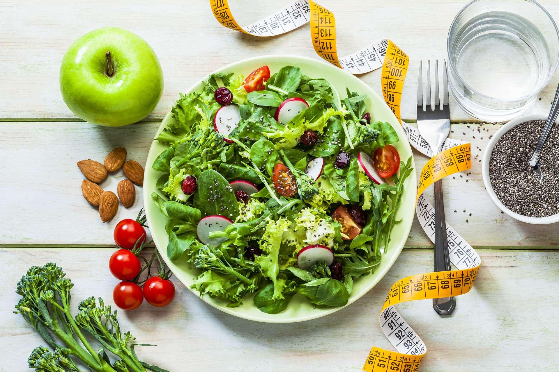 Großer frischer Salat, Apfel und Tomaten. Maßband. Frisches Gemüse. Konzept für Abnehmen und Diät. Vegane Ernährung.