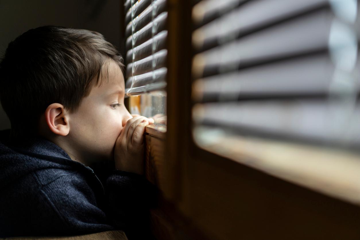 Kleiner trauriger Junge, der durch das Fenster schaut. Konzept zur sozialen Distanzierung bei Coronavirus-Pandemie