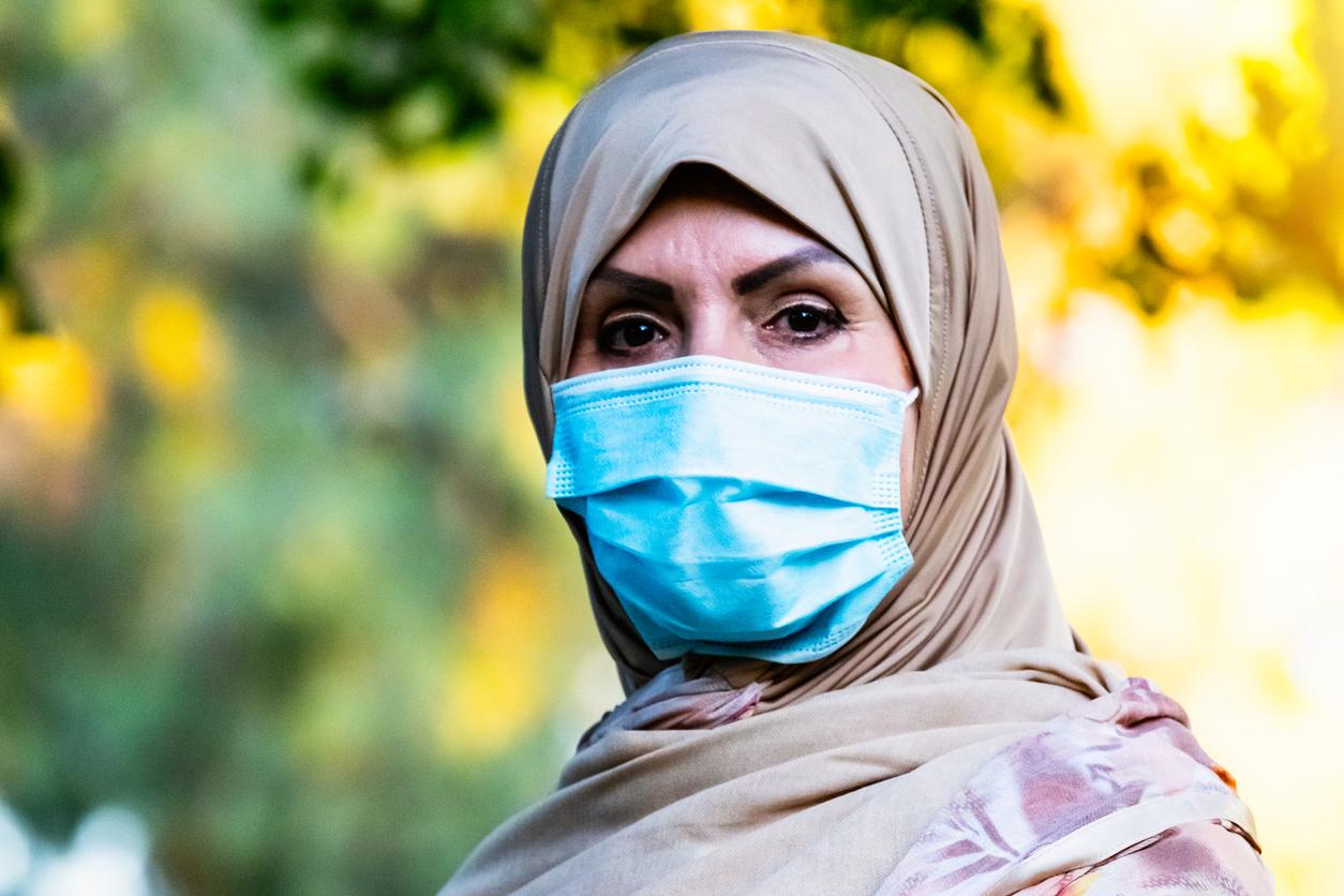 Lächelnde reife nahöstliche muslimische Frau, die die Kamera mit einer schützenden Gesichtsmaske betrachtet