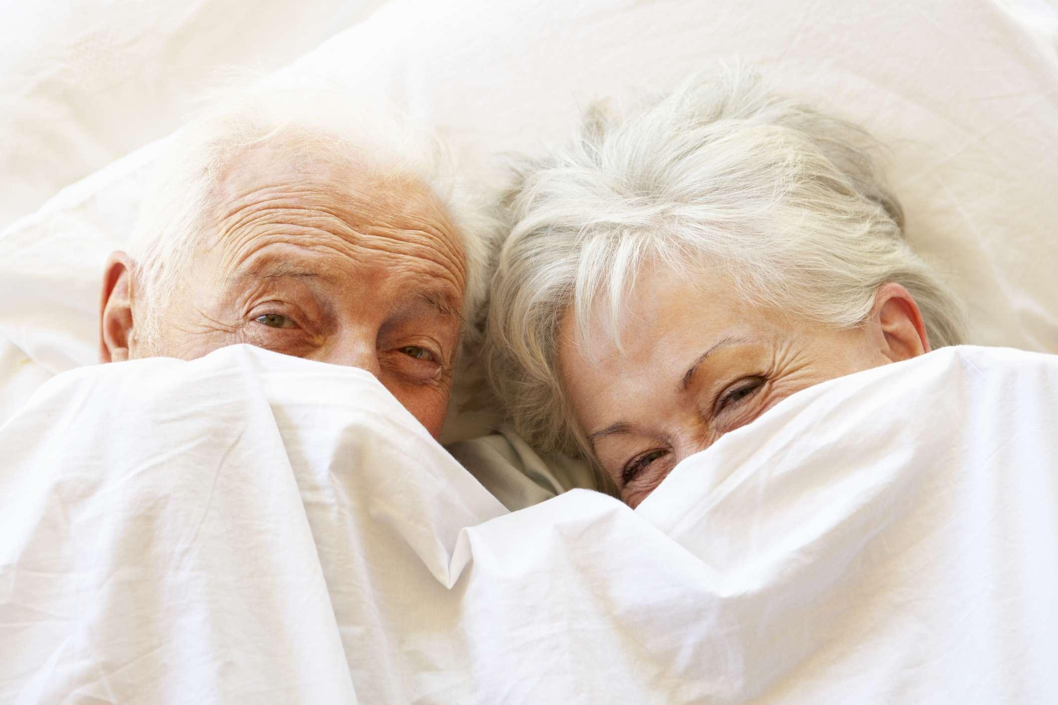 Älteres Paar, das sich im Bett versteckt, das unter Laken lächelt und lacht.