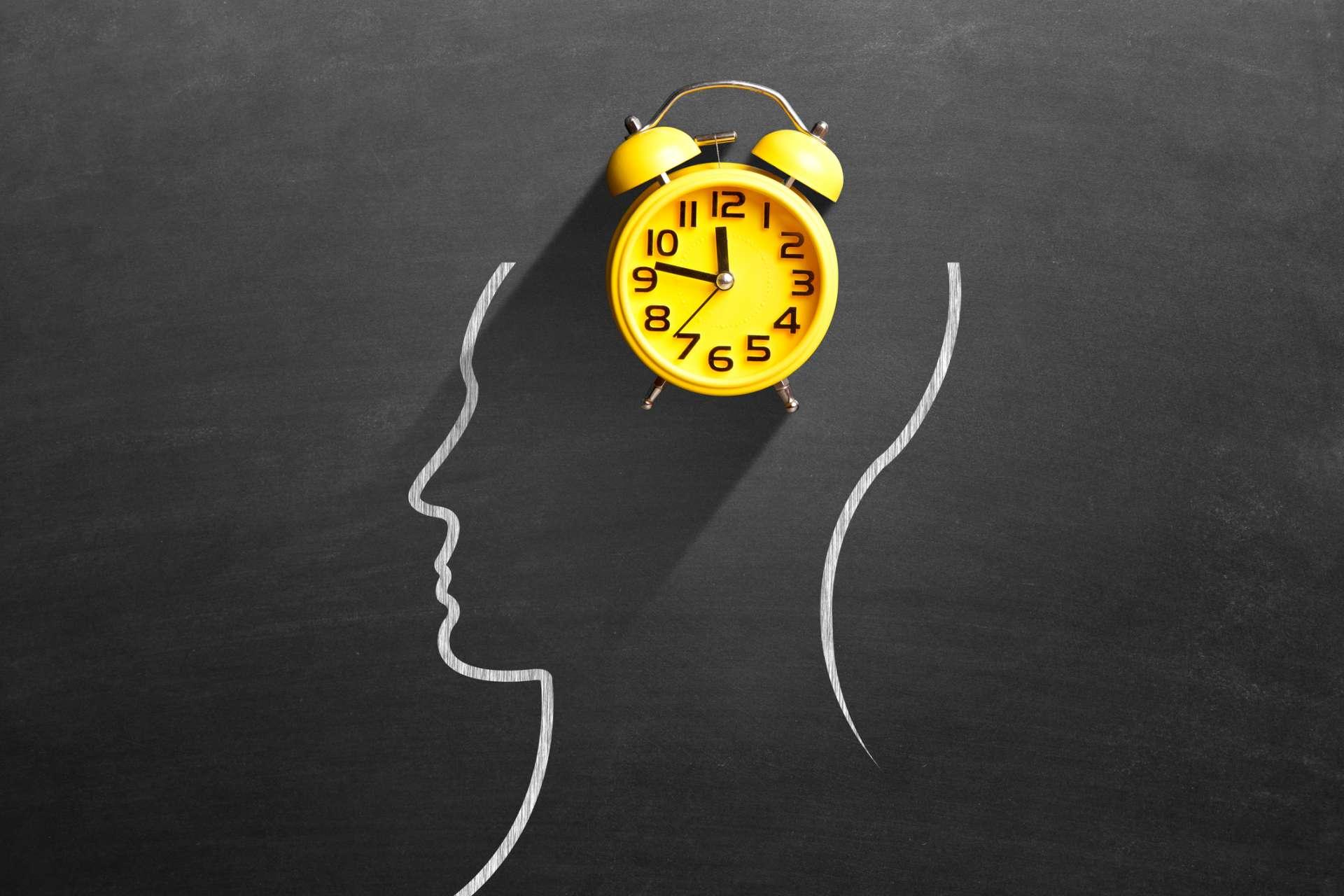 Gelber Wecker vor dem menschlichen Gehirn auf der Tafel, der das Konzept des Zeitmanagements darstellt.