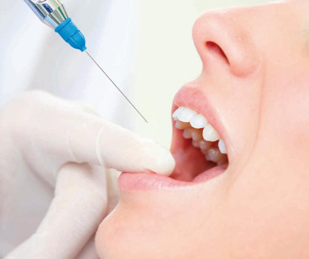 Zahnarzt hält eine Spritze und betäubt seinen Patienten