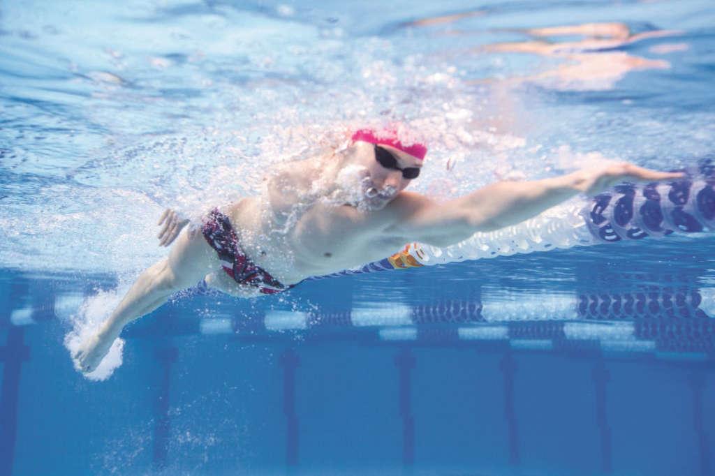 Underwated photo of a young muscular man swimming front crawl style through the olympic swimming pool.
