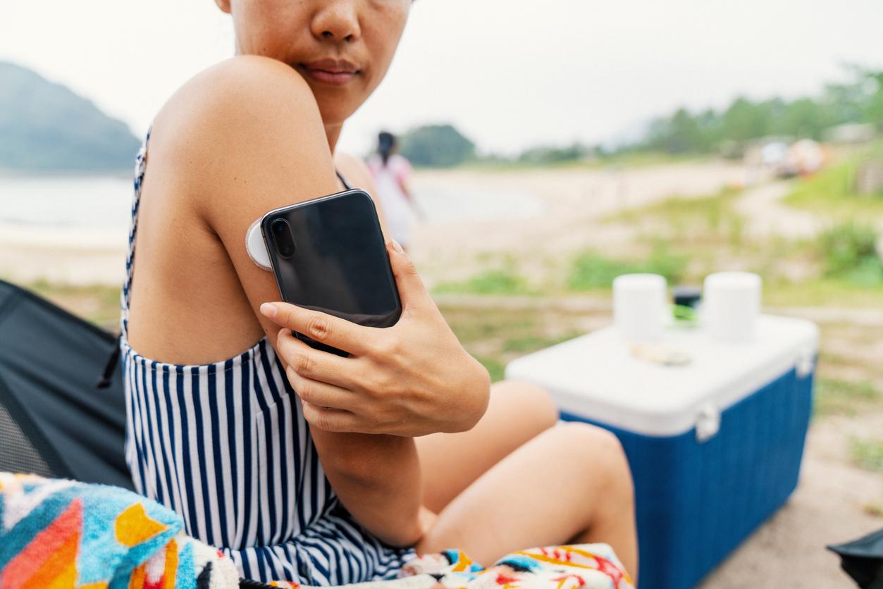 Woman at the beach wearing a glucose tracking sensor checking her level using an app. Tottori, Japan