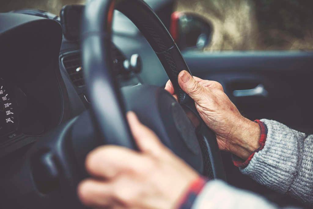 Hände einer alten Person am Lenkrad eines Auto