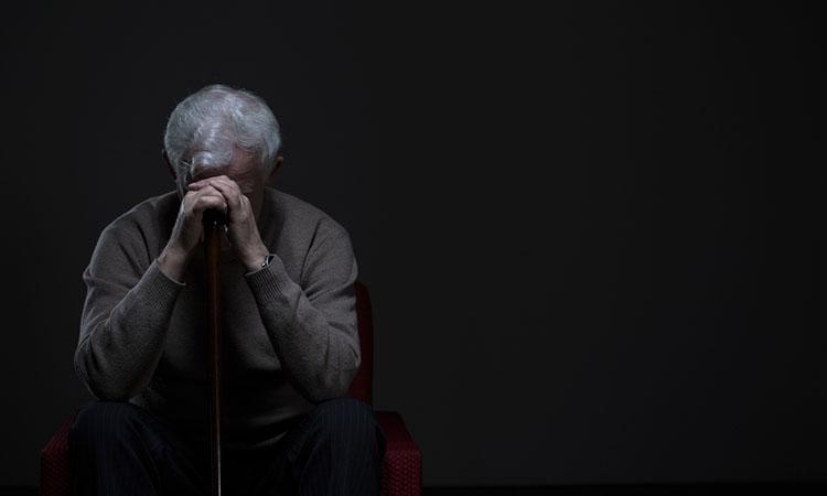 Deprimierter alter Mann versteckt sein Gesicht hinter seinen auf einem Stock aufgestützten Händen