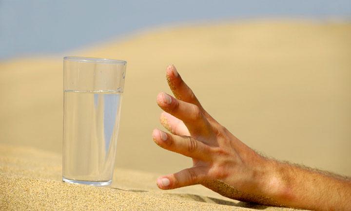 Hand is reaching for a fresh glass of cold water in desert.