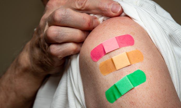 Alte Person zieht seinen Ärmel hoch und zeigt drei farbige Pflaster von Impfungen auf dem Oberarm
