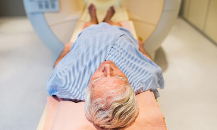 Senior receiving an MRI Scan for prostate cancer. Focus is on foreground.