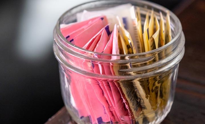 small glass bowl full of assorted artificial sweetener envelopes