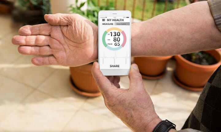 An elderly man measures blood pressure and pulse by mobile phone with medical application