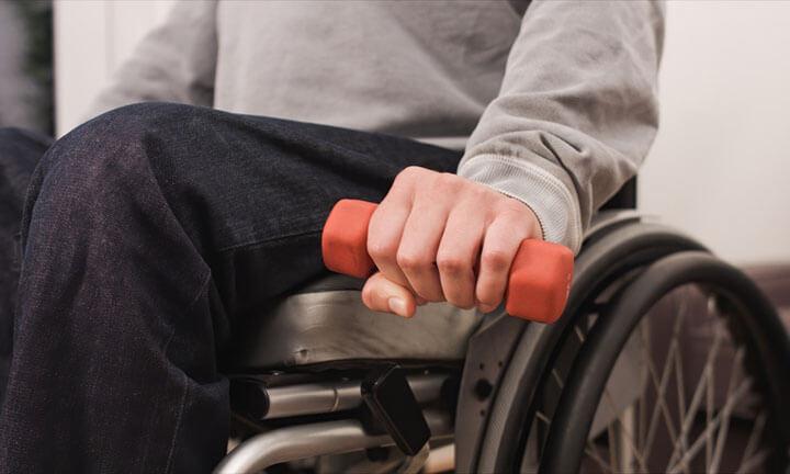 Man in wheelchair exercising and lifting weight in a living room.