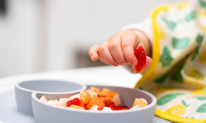 Macro Close up of Baby Hand with a Piece of Fruits Sitting in Child's Chair Kid Eating Healthy Food