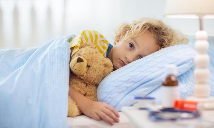 Kleines Kind liegt krank mit Teddy im Bett