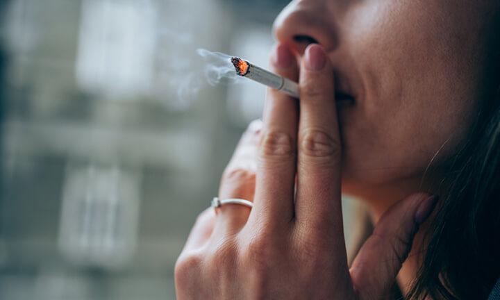 Unerkennbare junge Frau raucht am Fenster eine Zigarette