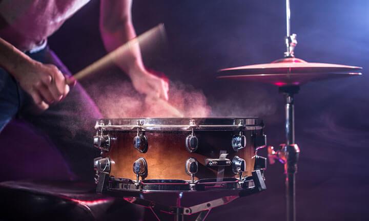 Ein unerkennbarer Schlagzeuger spielt im rot-blauen Stimmungslicht auf einer Snare Drum
