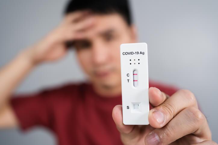 junger gestresster Mann mit positivem Coronavirus(Covid-19)-Testergebnis mit Antigen-Schnelltest-Kit (ATK)